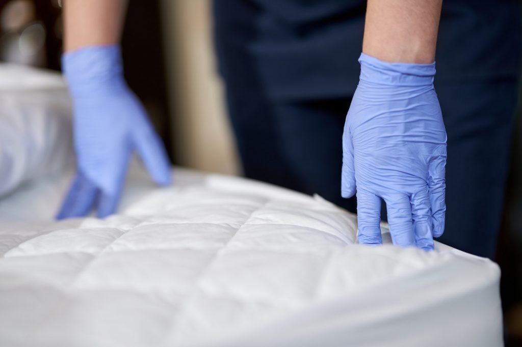 Maid in gloves touching the mattress by hands